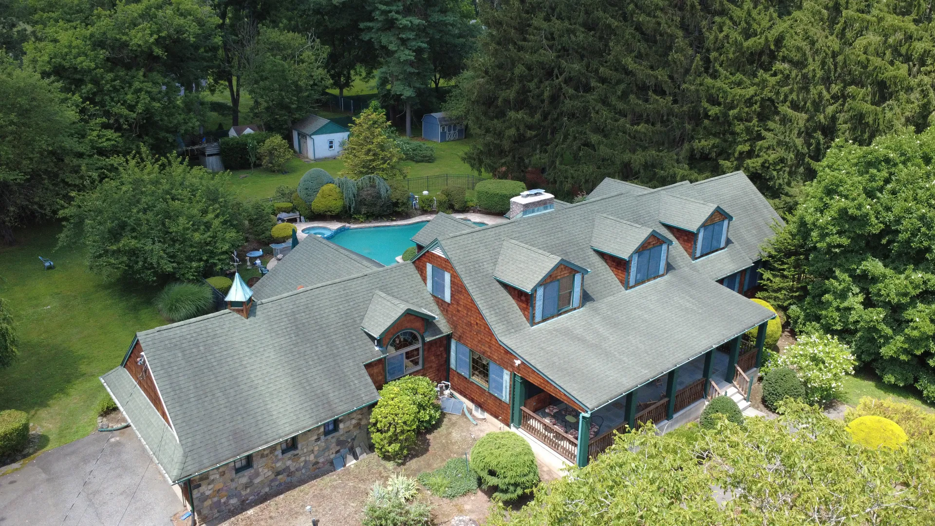Aerial view of a shingled New Jersey house on a wooded lot, showing the roof line, rear deck and grounds