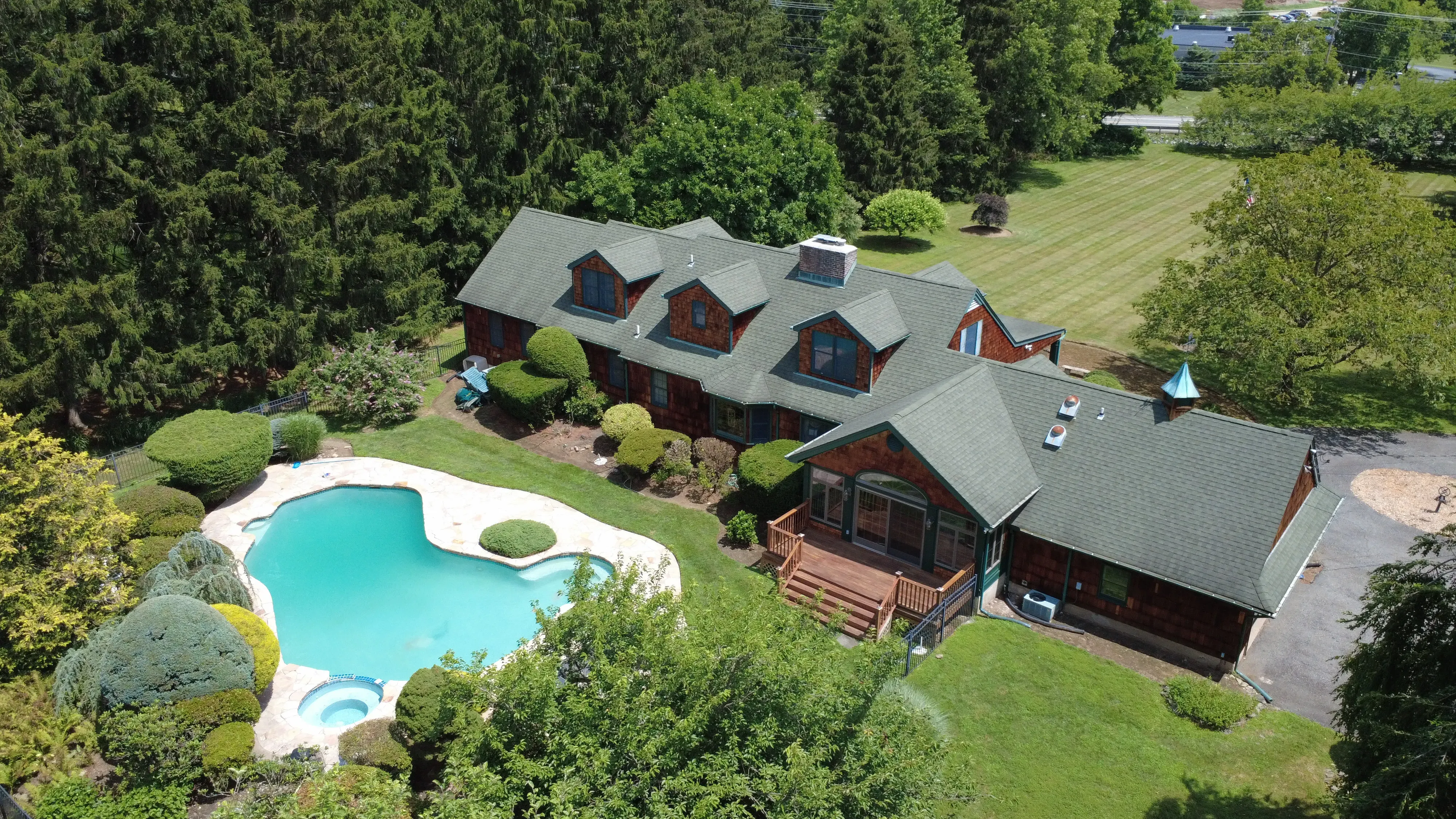 Aerial view of a cedar-shingled New Jersey house on a wooded lot, showing the roof, a pool and the surrounding grounds